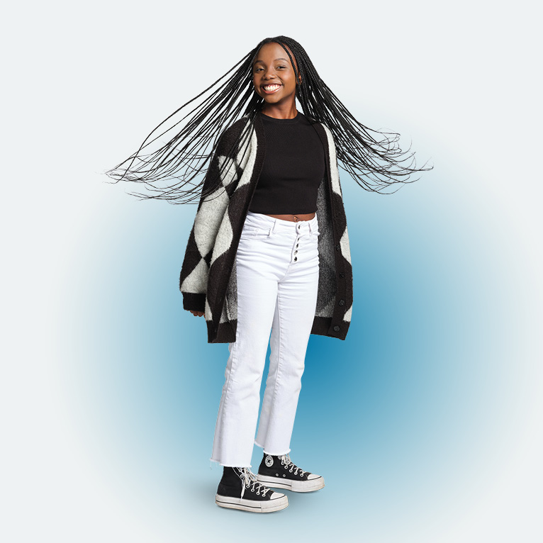 Full body photo of Lynn Mwongela smiling at the camera with her braids in motion around her head, in a black shirt, white jeans, and black and white cardigan, on a white background.
