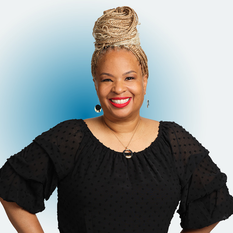 Cropped portrait of screenwriter and LMU faculty member Michelle Amor Gillie with her braids piled on her head in a bun, black blouse, with hands on her hips on a white background